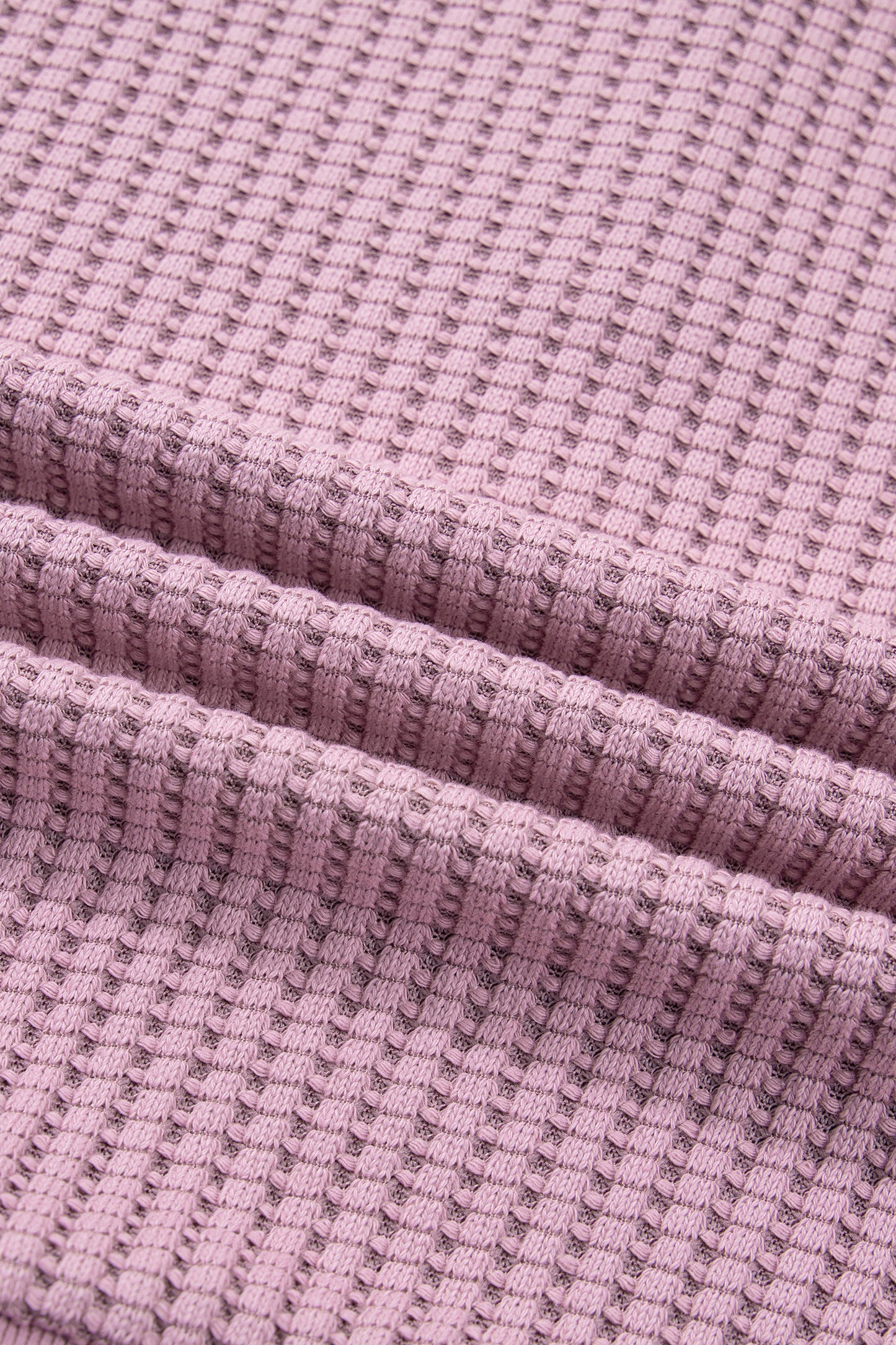 Woman wearing a Blush textured waffle knit pullover with snap collar, relaxed long sleeves, and ribbed cuffs with white pants.