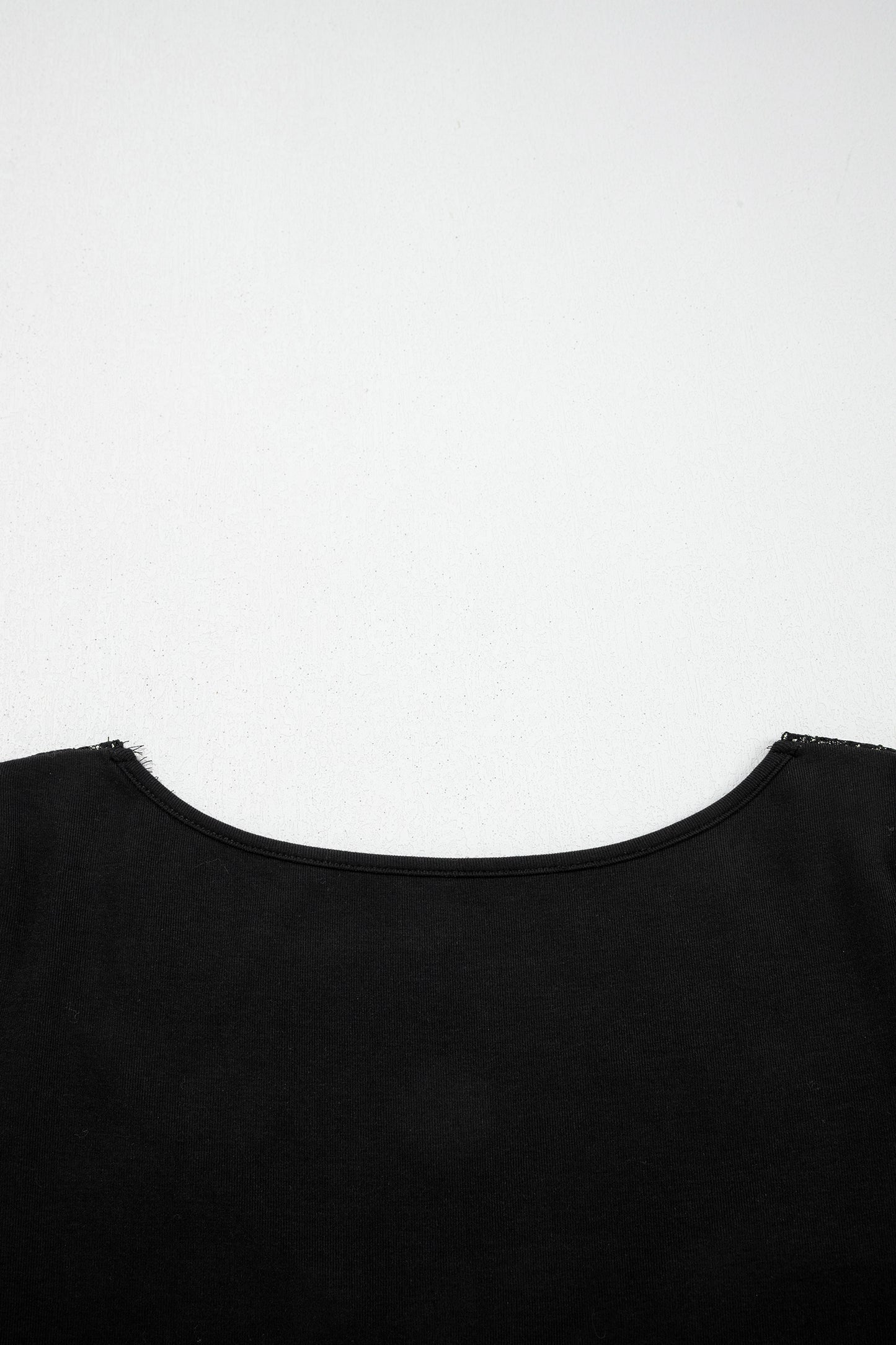 Black fitted long sleeve top with floral lace-trim V-neckline and soft stretch fabric styled with white pants.