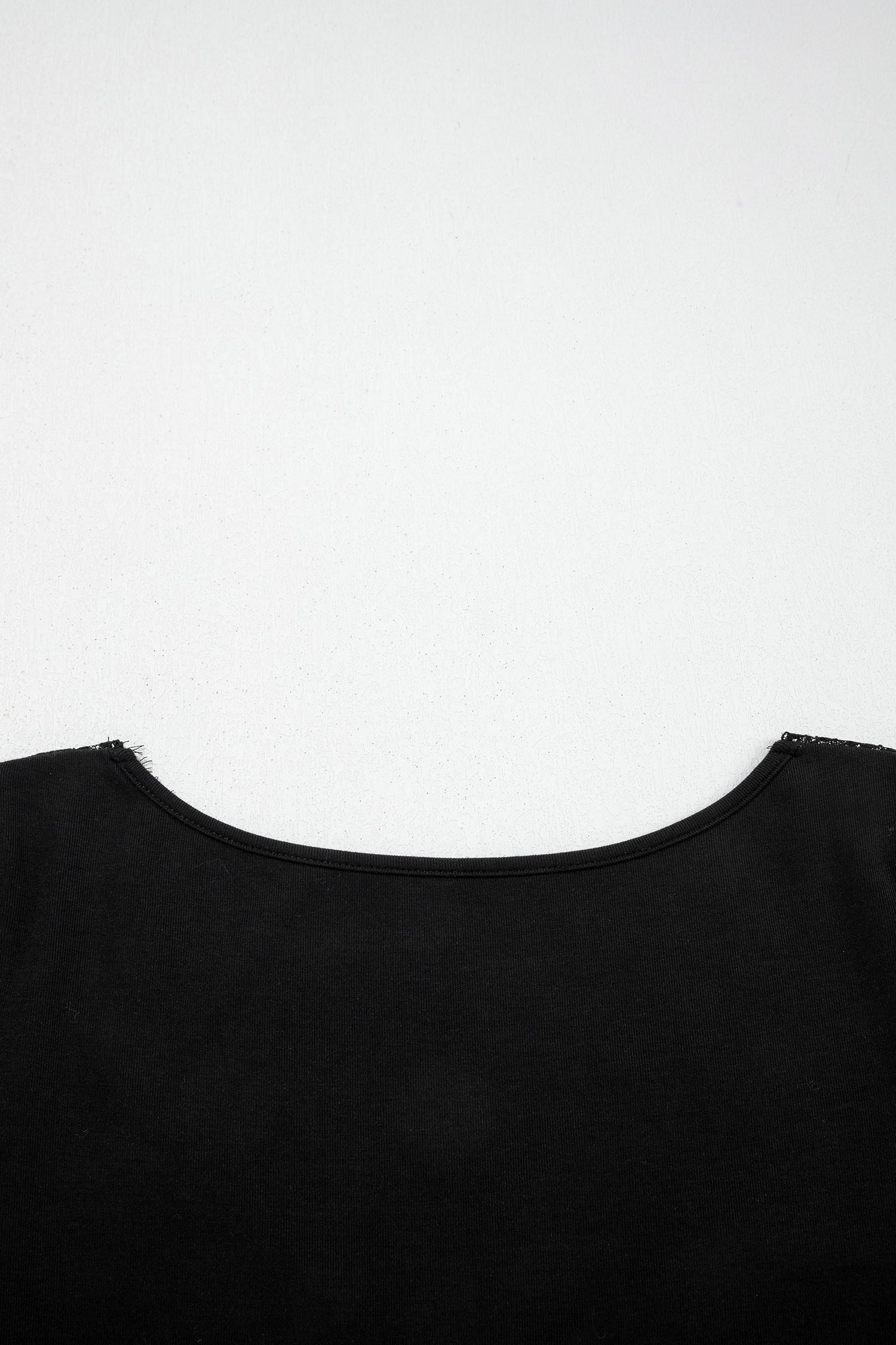 Black fitted long sleeve top with floral lace-trim V-neckline and soft stretch fabric styled with white pants.