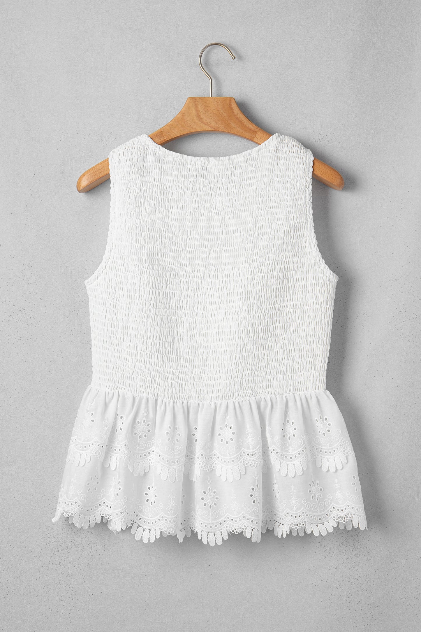 Women's white smocked sleeveless peplum top with embroidered eyelet hem, round neckline, textured bodice, and feminine boutique style.