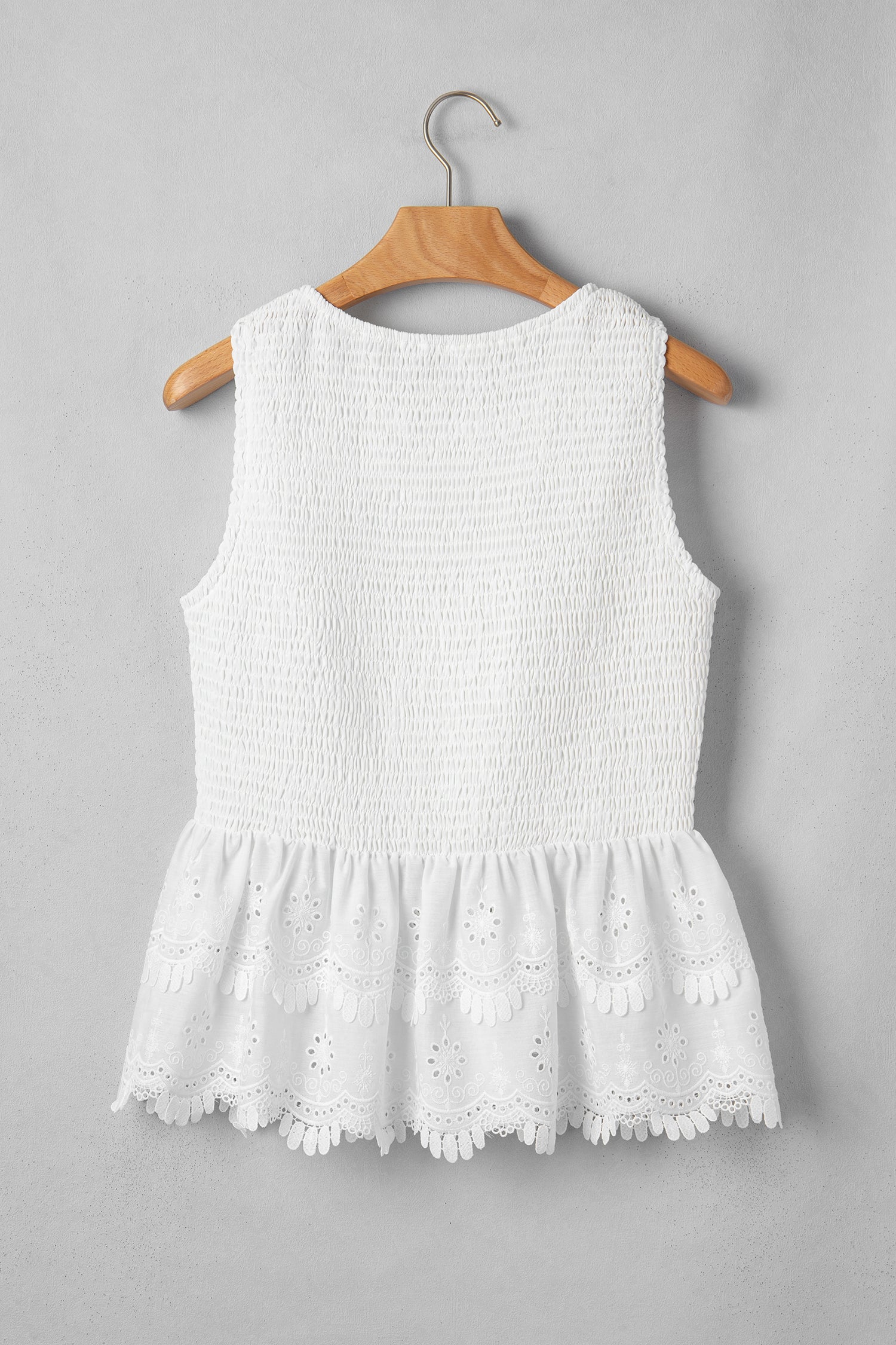 Women's white smocked sleeveless peplum top with embroidered eyelet hem, round neckline, textured bodice, and feminine boutique style.