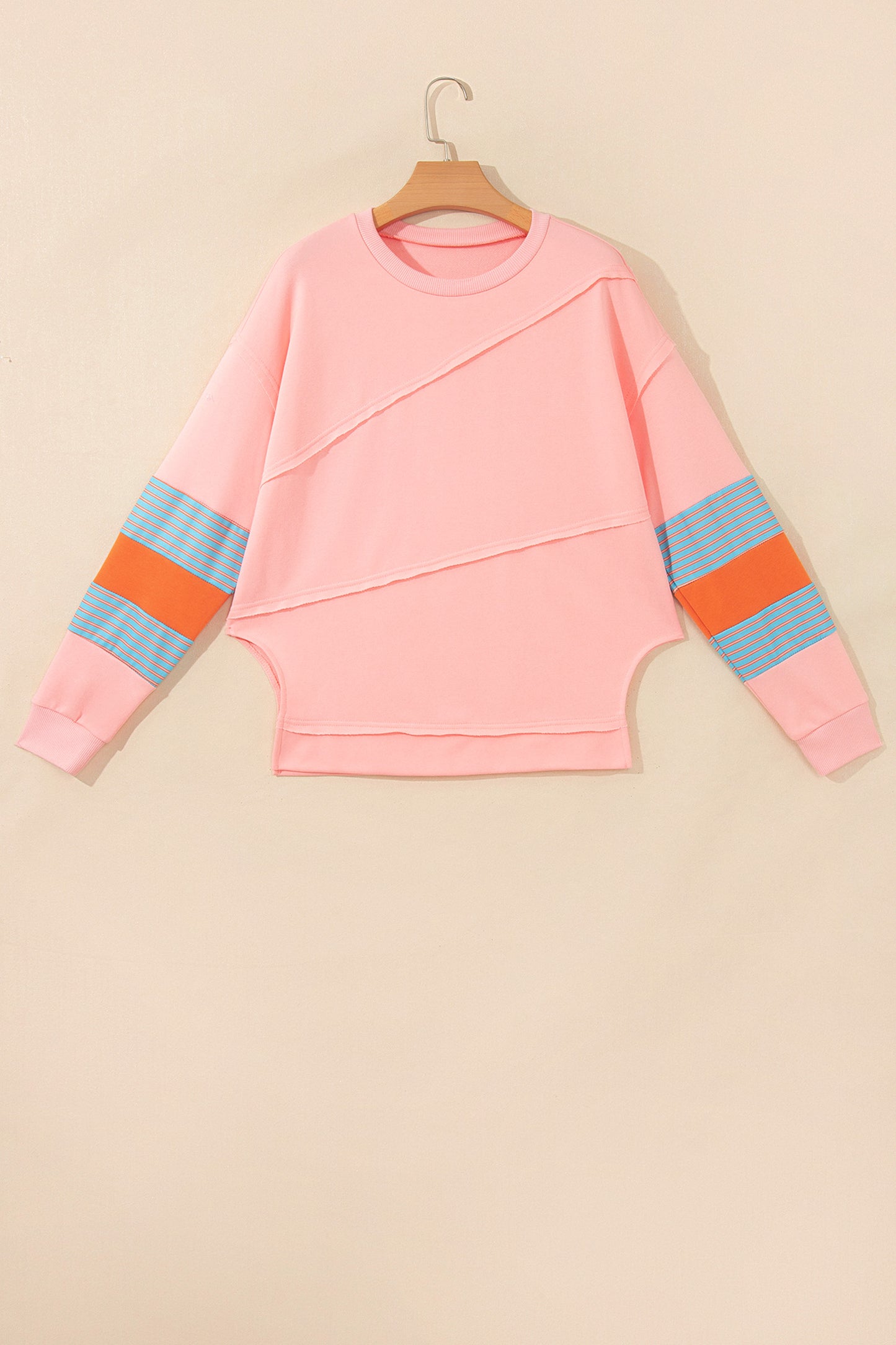 Pink crew neck long sleeve top with asymmetrical paneled body design and blue striped color block sleeves with contrasting orange accents.