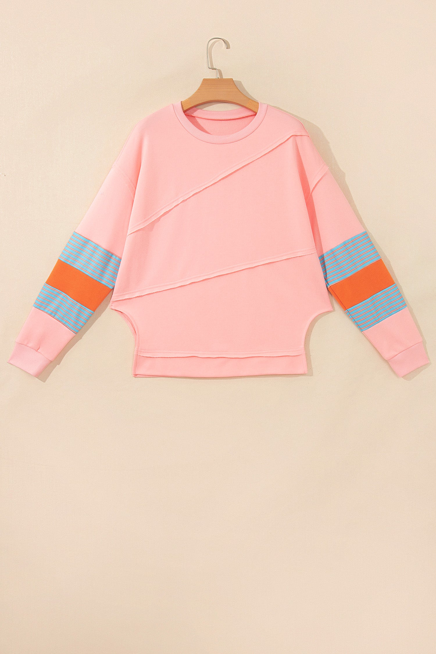 Pink crew neck long sleeve top with asymmetrical paneled body design and blue striped color block sleeves with contrasting orange accents.