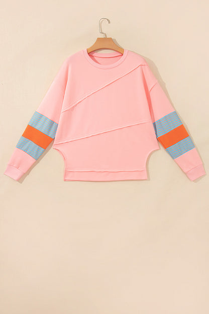 Pink crew neck long sleeve top with asymmetrical paneled body design and blue striped color block sleeves with contrasting orange accents.