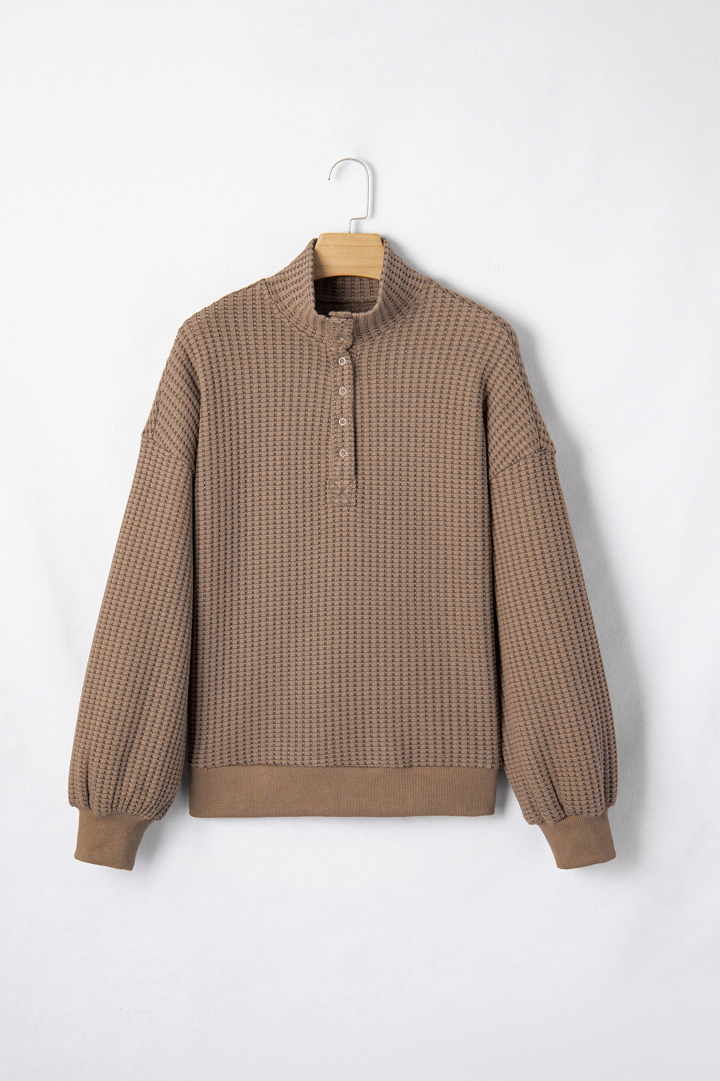Woman wearing a Mocha textured waffle knit pullover with snap collar, relaxed long sleeves, and ribbed cuffs with white pants.