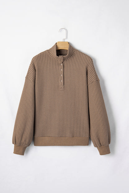 Woman wearing a Mocha textured waffle knit pullover with snap collar, relaxed long sleeves, and ribbed cuffs with white pants.