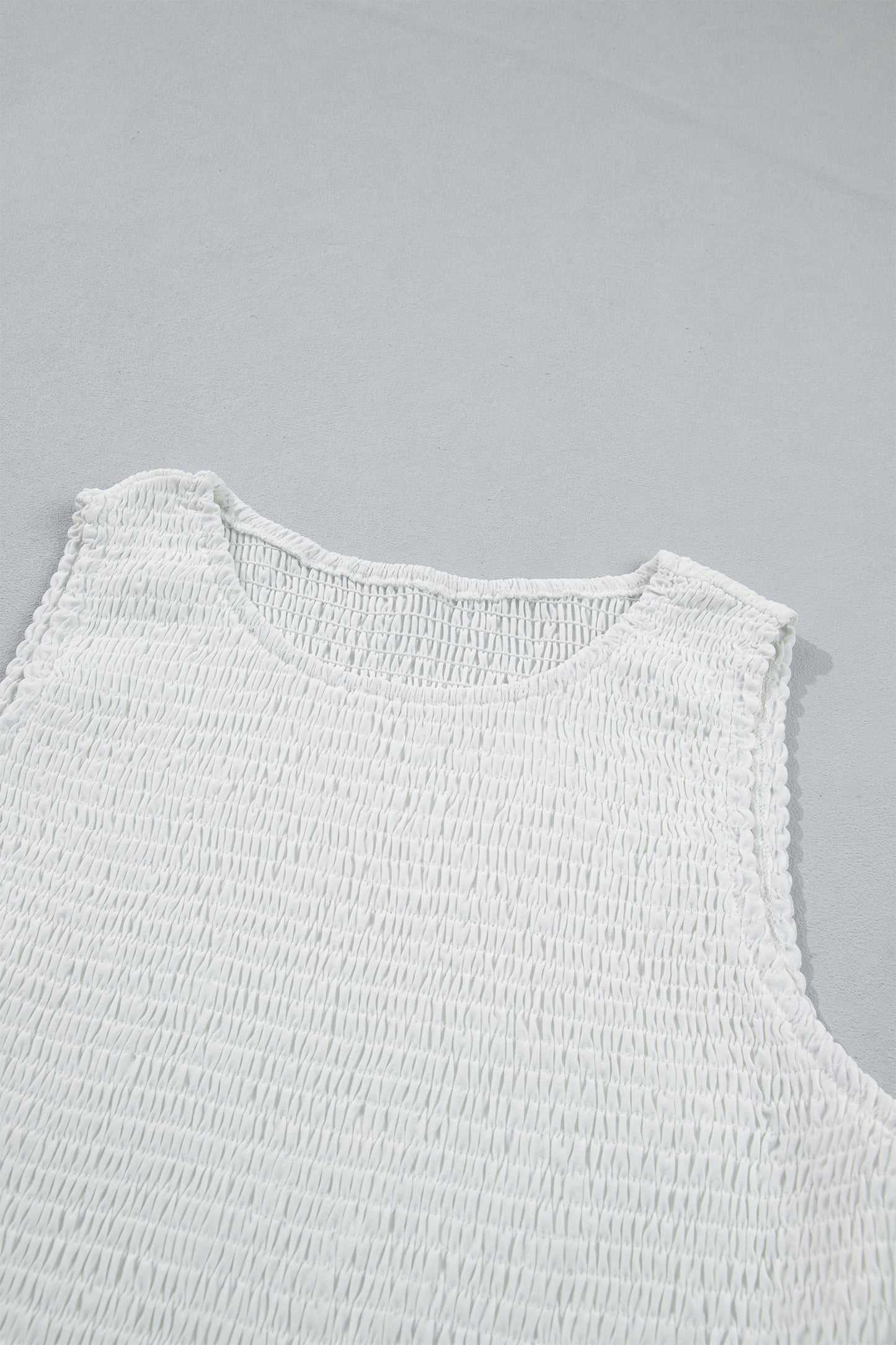 Women's white smocked sleeveless peplum top with embroidered eyelet hem, round neckline, textured bodice, and feminine boutique style.