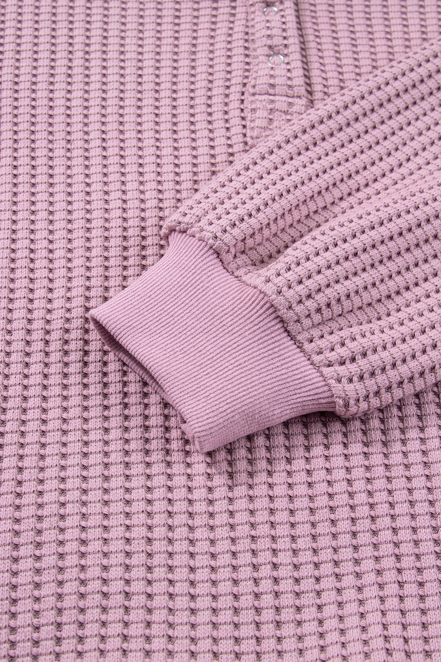 Woman wearing a Blush textured waffle knit pullover with snap collar, relaxed long sleeves, and ribbed cuffs with white pants.