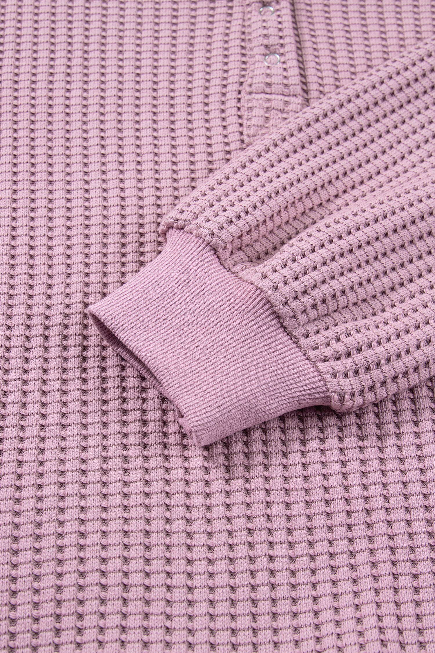 Woman wearing a Blush textured waffle knit pullover with snap collar, relaxed long sleeves, and ribbed cuffs with white pants.