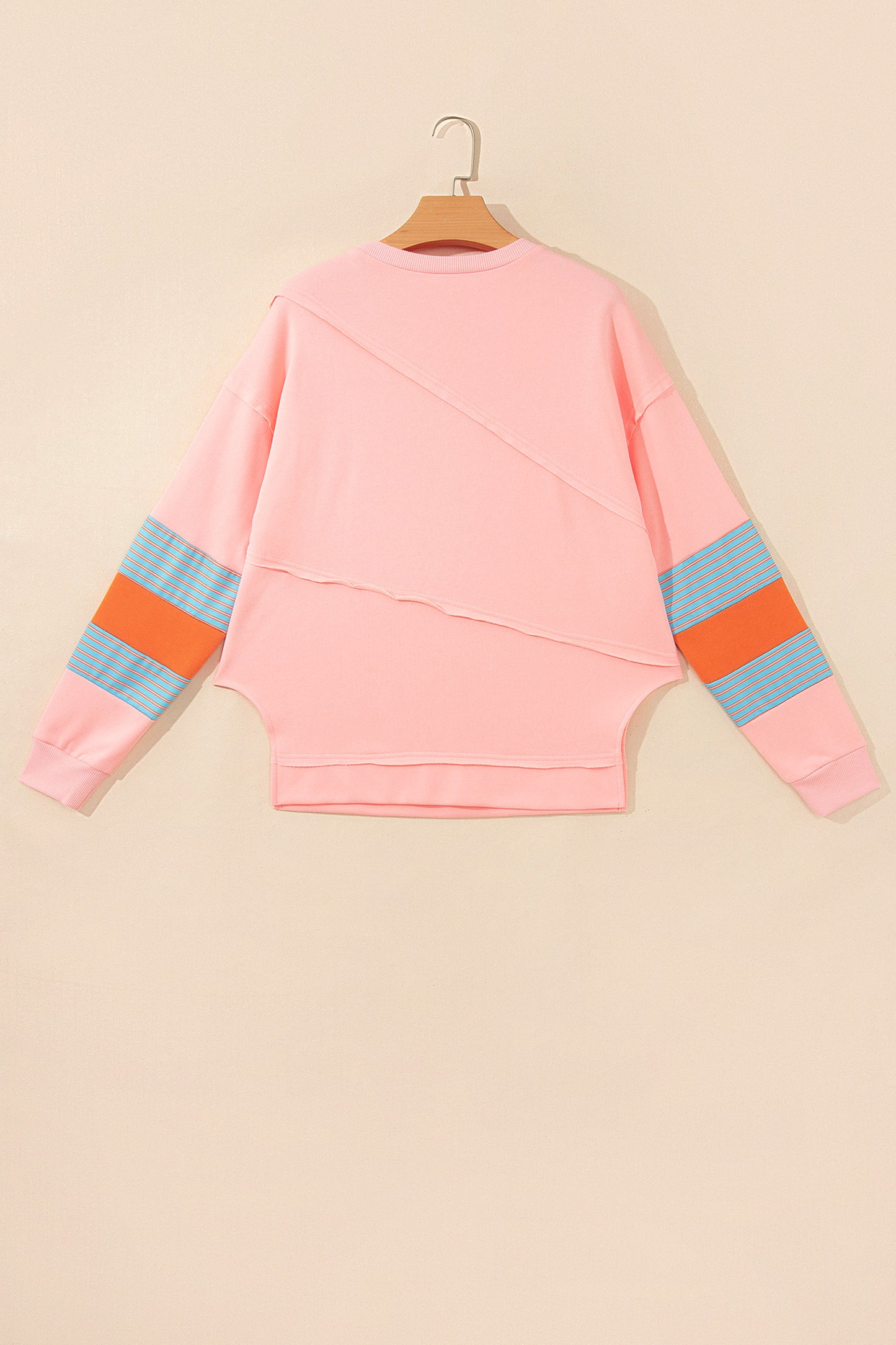 Pink crew neck long sleeve top with asymmetrical paneled body design and blue striped color block sleeves with contrasting orange accents.