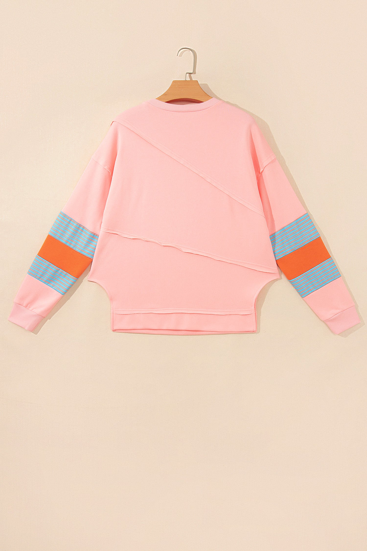 Pink crew neck long sleeve top with asymmetrical paneled body design and blue striped color block sleeves with contrasting orange accents.