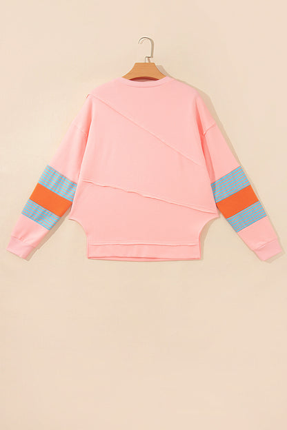 Pink crew neck long sleeve top with asymmetrical paneled body design and blue striped color block sleeves with contrasting orange accents.