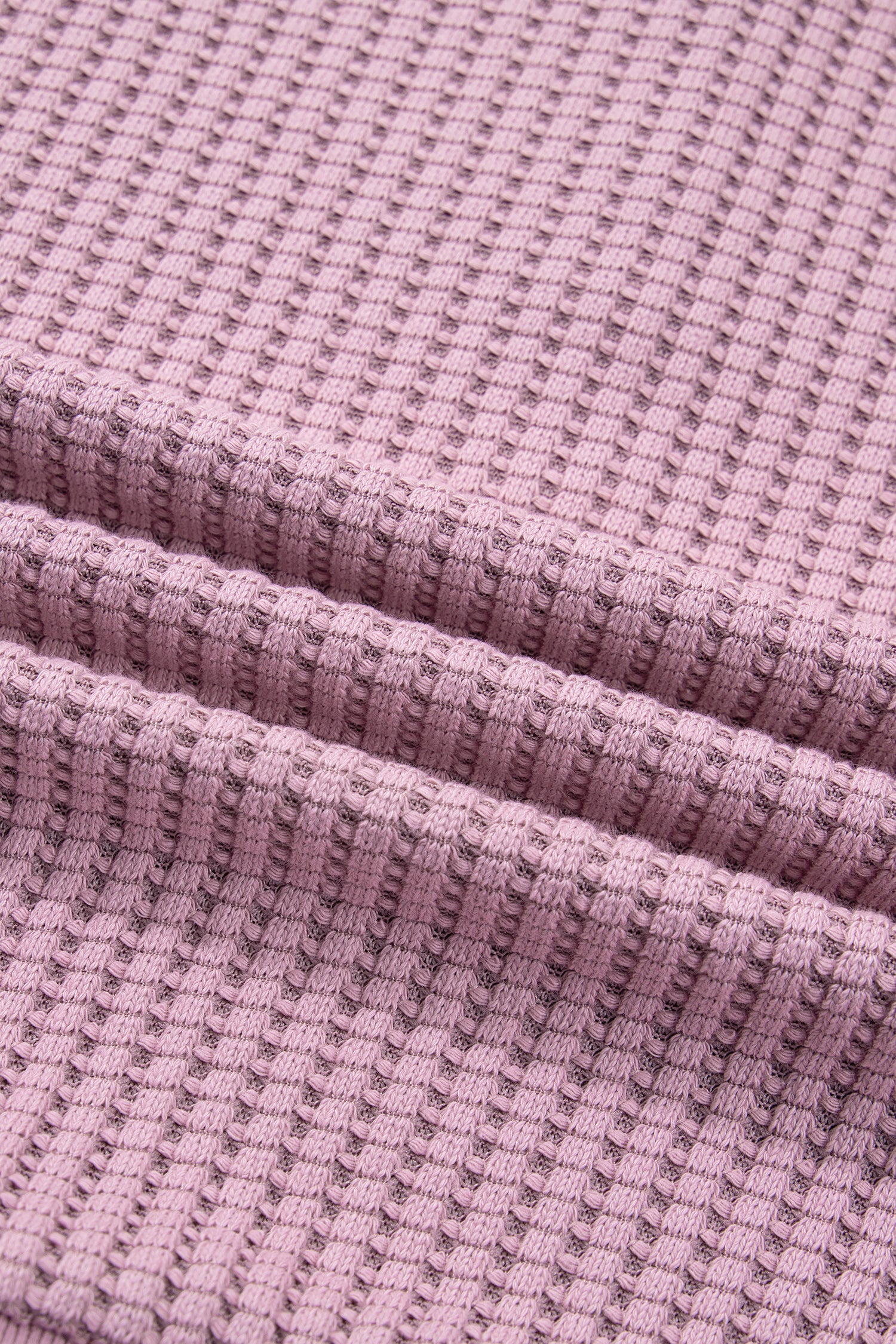 Woman wearing a Blush textured waffle knit pullover with snap collar, relaxed long sleeves, and ribbed cuffs with white pants.