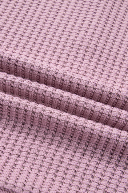 Woman wearing a Blush textured waffle knit pullover with snap collar, relaxed long sleeves, and ribbed cuffs with white pants.