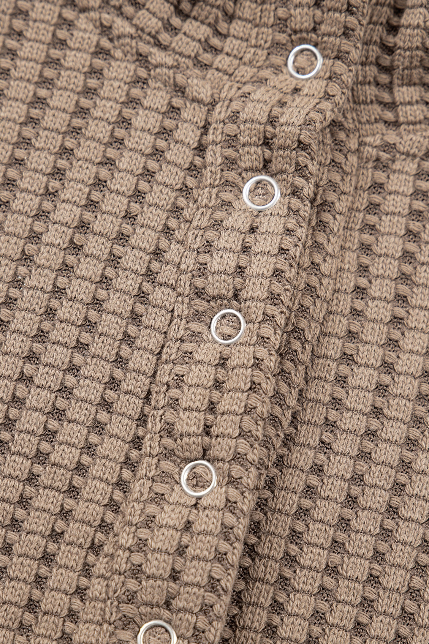 Woman wearing a Mocha textured waffle knit pullover with snap collar, relaxed long sleeves, and ribbed cuffs with white pants.