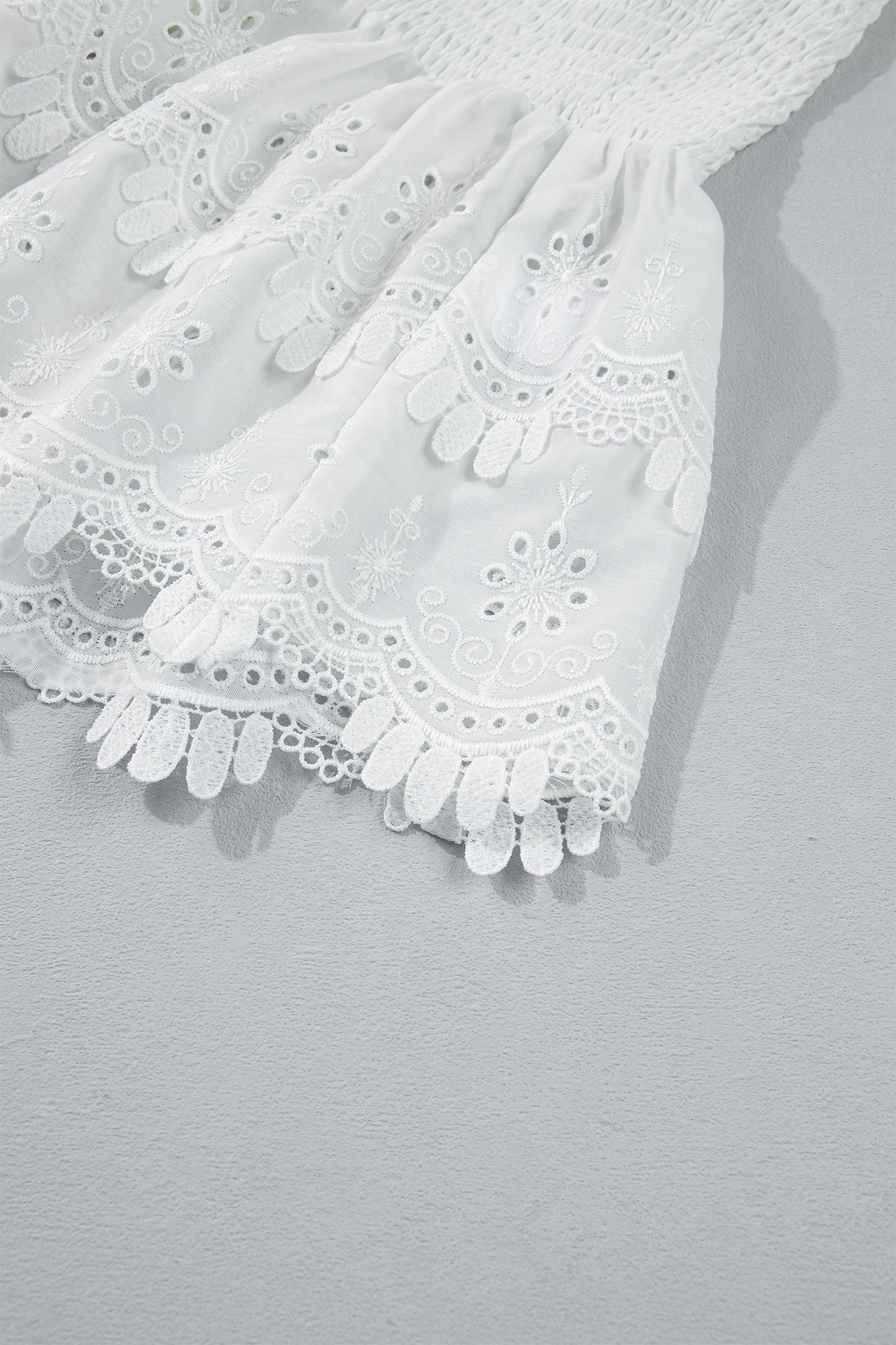 Women's white smocked sleeveless peplum top with embroidered eyelet hem, round neckline, textured bodice, and feminine boutique style.