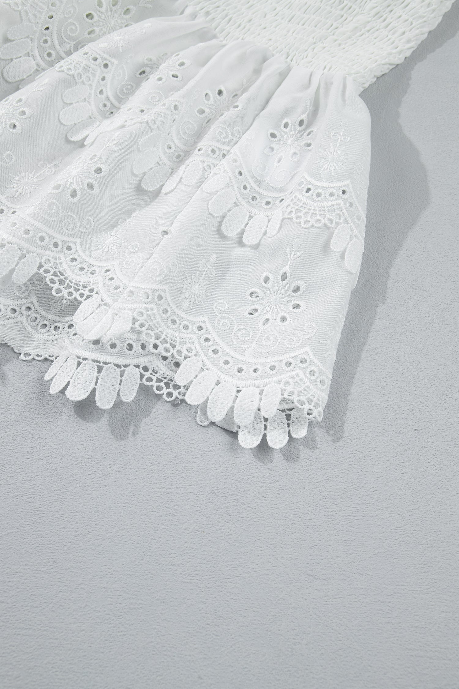 Women's white smocked sleeveless peplum top with embroidered eyelet hem, round neckline, textured bodice, and feminine boutique style.