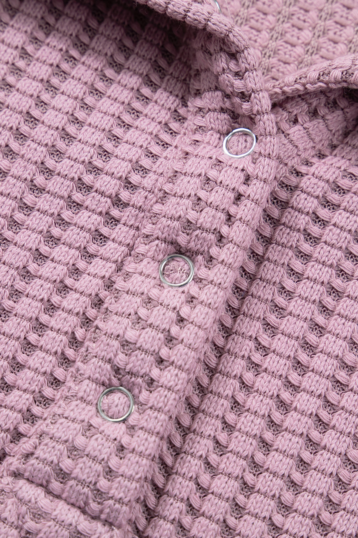 Woman wearing a Blush textured waffle knit pullover with snap collar, relaxed long sleeves, and ribbed cuffs with white pants.