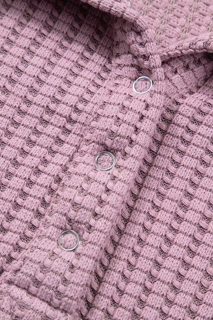 Woman wearing a Blush textured waffle knit pullover with snap collar, relaxed long sleeves, and ribbed cuffs with white pants.