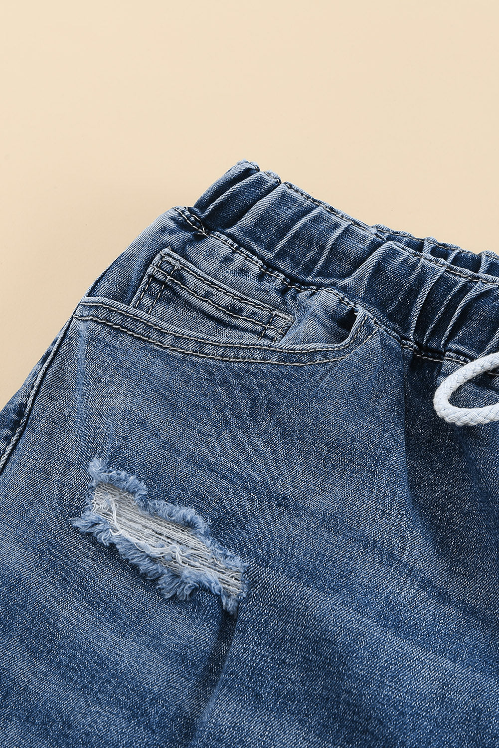 Medium wash blue distressed slim straight leg jeans with drawstring elastic waist and raw hem