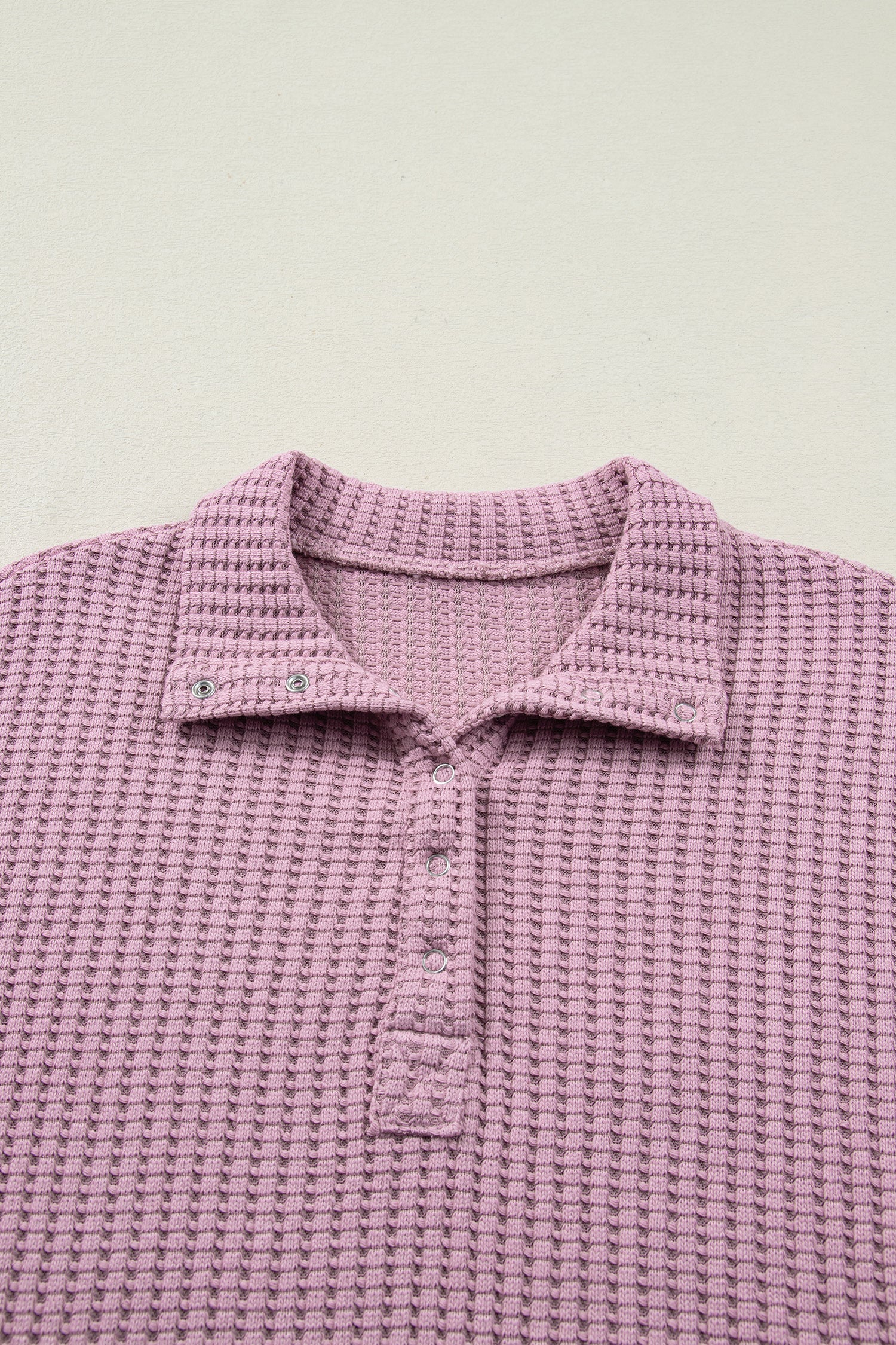Woman wearing a Blush textured waffle knit pullover with snap collar, relaxed long sleeves, and ribbed cuffs with white pants.
