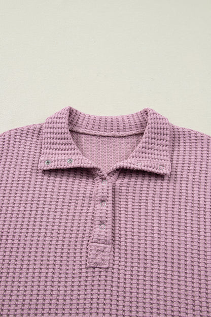 Woman wearing a Blush textured waffle knit pullover with snap collar, relaxed long sleeves, and ribbed cuffs with white pants.