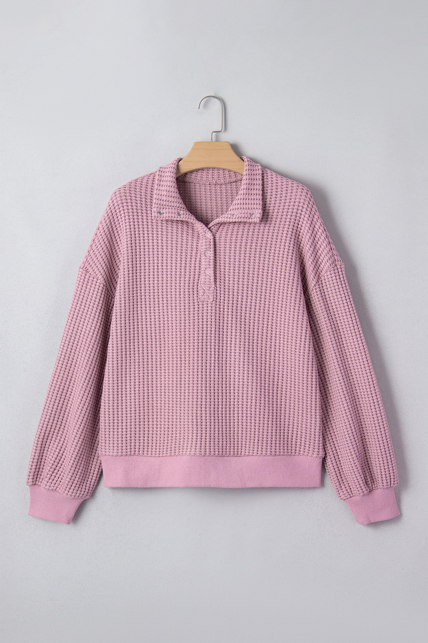 Woman wearing a Blush textured waffle knit pullover with snap collar, relaxed long sleeves, and ribbed cuffs with white pants.