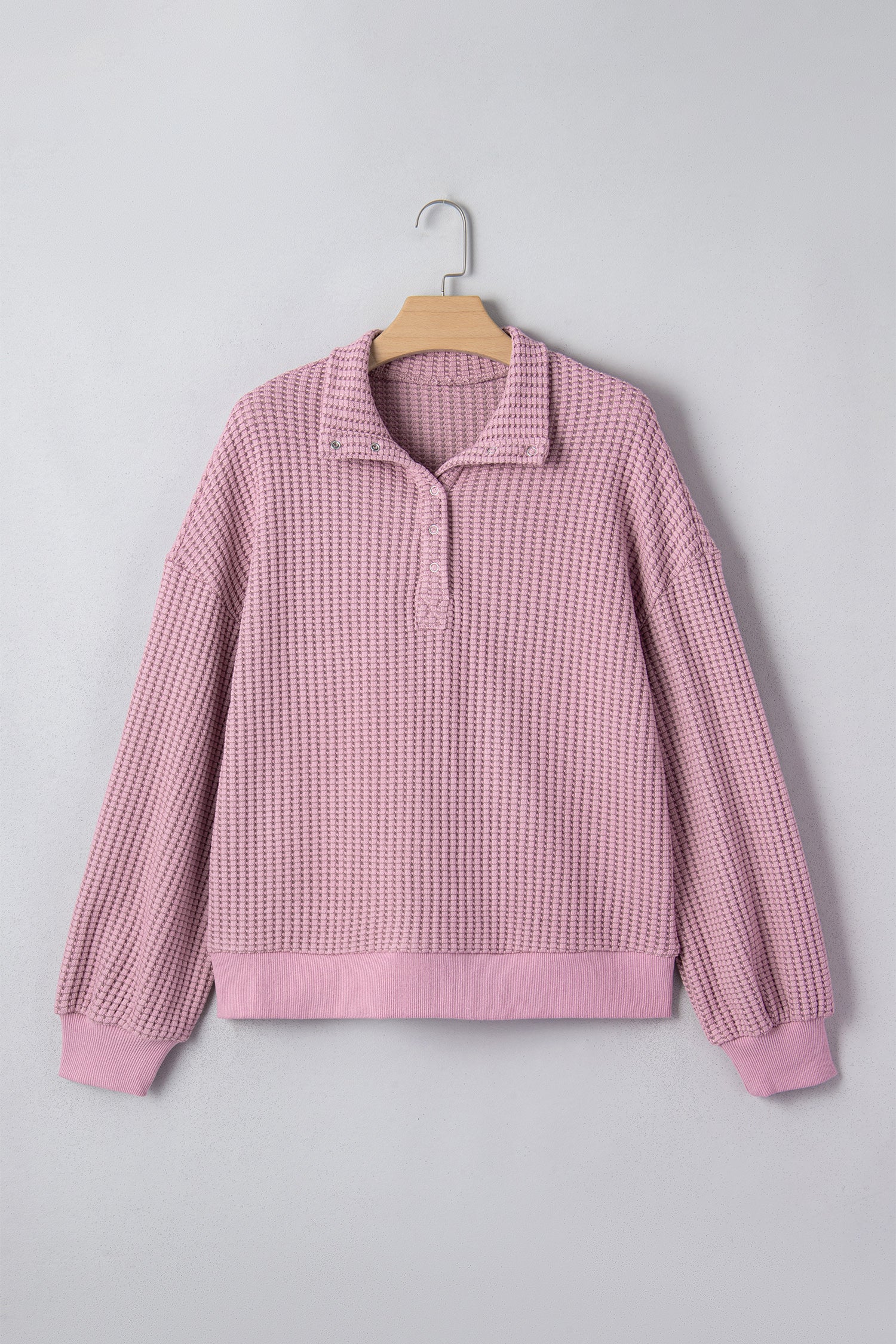Woman wearing a Blush textured waffle knit pullover with snap collar, relaxed long sleeves, and ribbed cuffs with white pants.