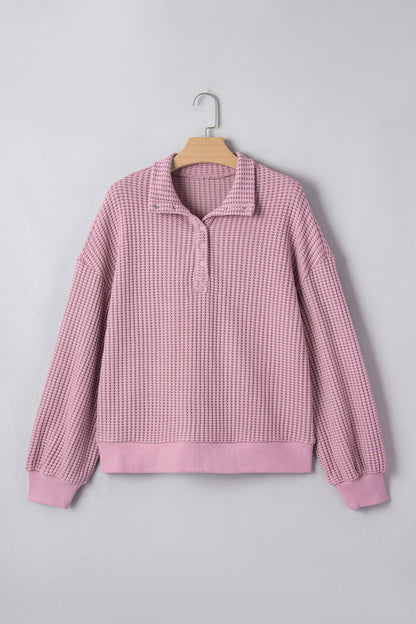 Woman wearing a Blush textured waffle knit pullover with snap collar, relaxed long sleeves, and ribbed cuffs with white pants.