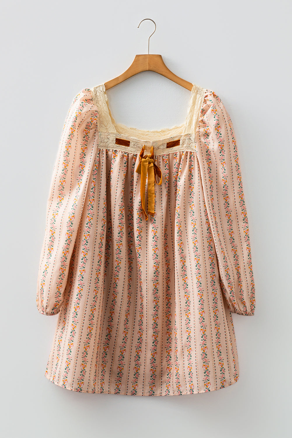 Blush floral babydoll mini dress with floral stripe print, cream lace-trimmed square neckline, brown velvet bow, and long sleeves.