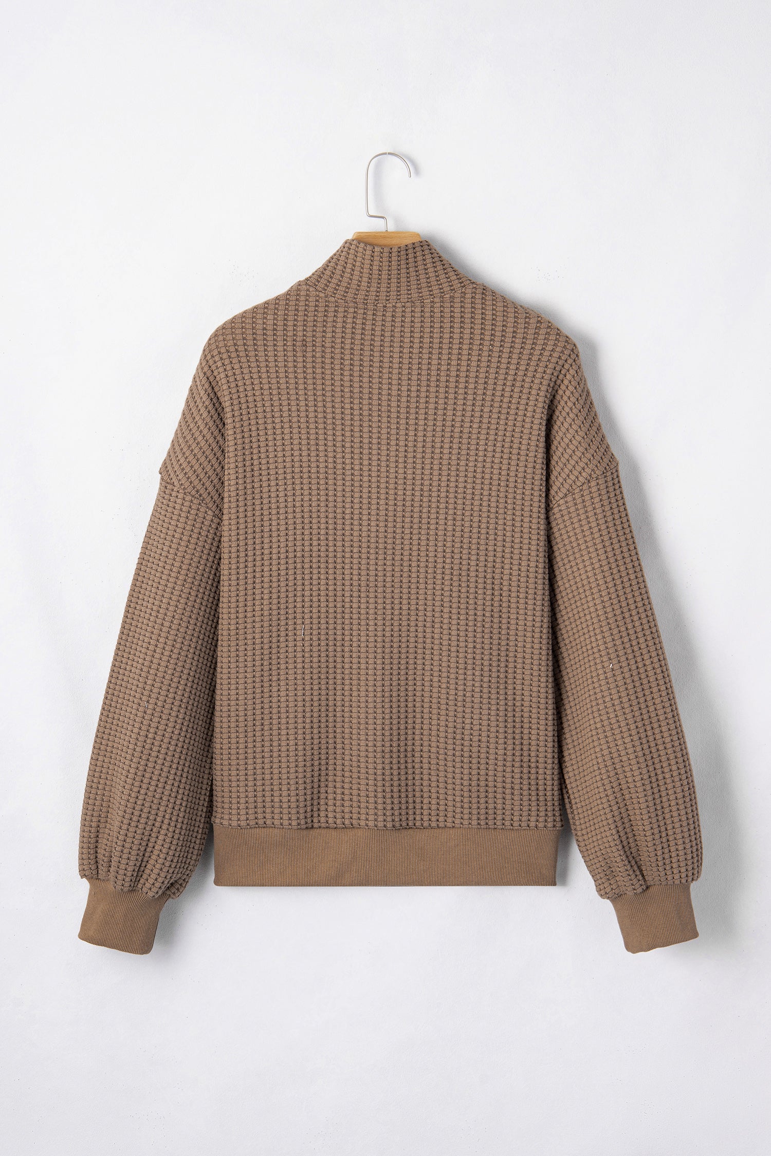 Woman wearing a Mocha textured waffle knit pullover with snap collar, relaxed long sleeves, and ribbed cuffs with white pants.