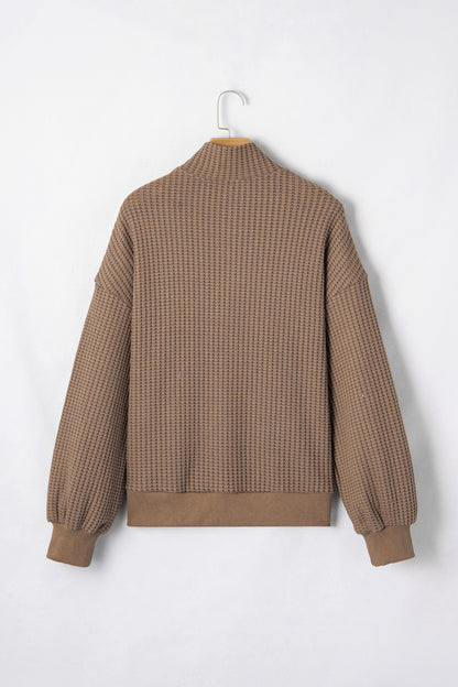 Woman wearing a Mocha textured waffle knit pullover with snap collar, relaxed long sleeves, and ribbed cuffs with white pants.