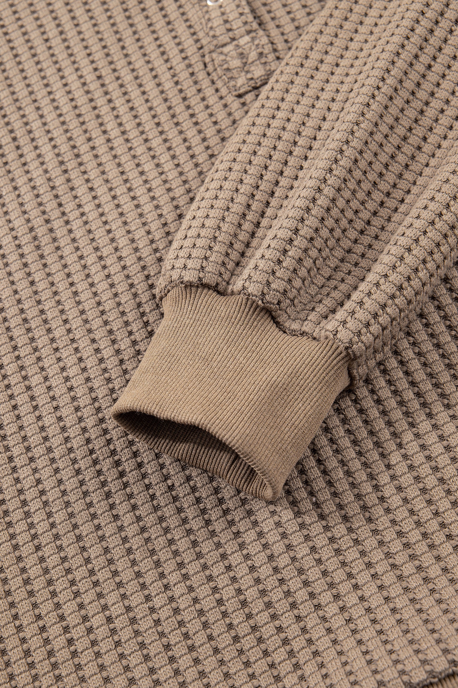 Woman wearing a Mocha textured waffle knit pullover with snap collar, relaxed long sleeves, and ribbed cuffs with white pants.