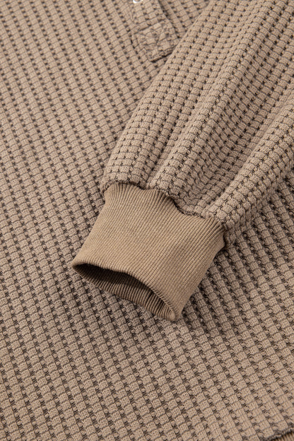 Woman wearing a Mocha textured waffle knit pullover with snap collar, relaxed long sleeves, and ribbed cuffs with white pants.