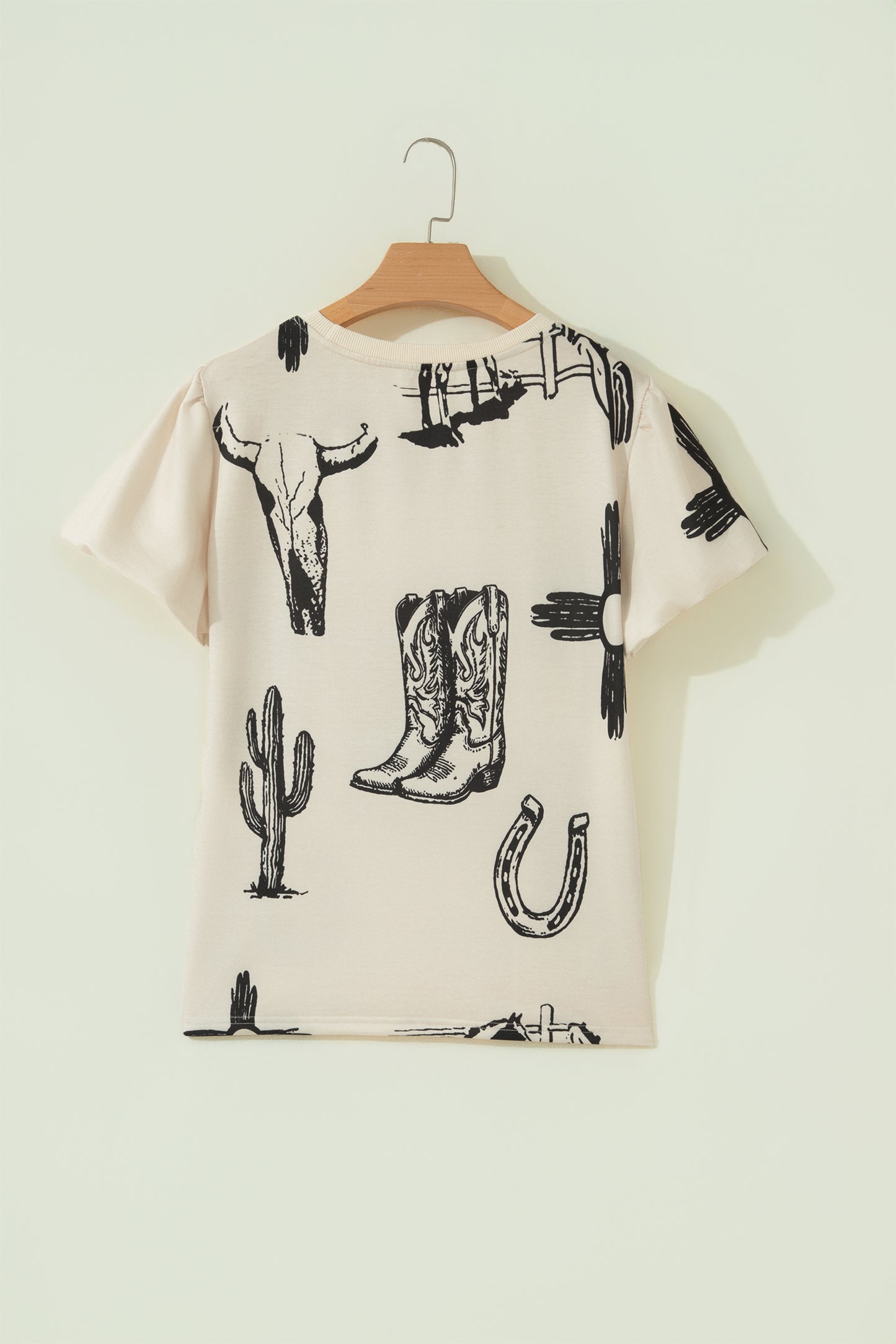 Cream Western graphic print top with crew neckline, short sleeves with gathered armholes, and black cowboy boot, cactus, horseshoe, and Southwestern motifs.