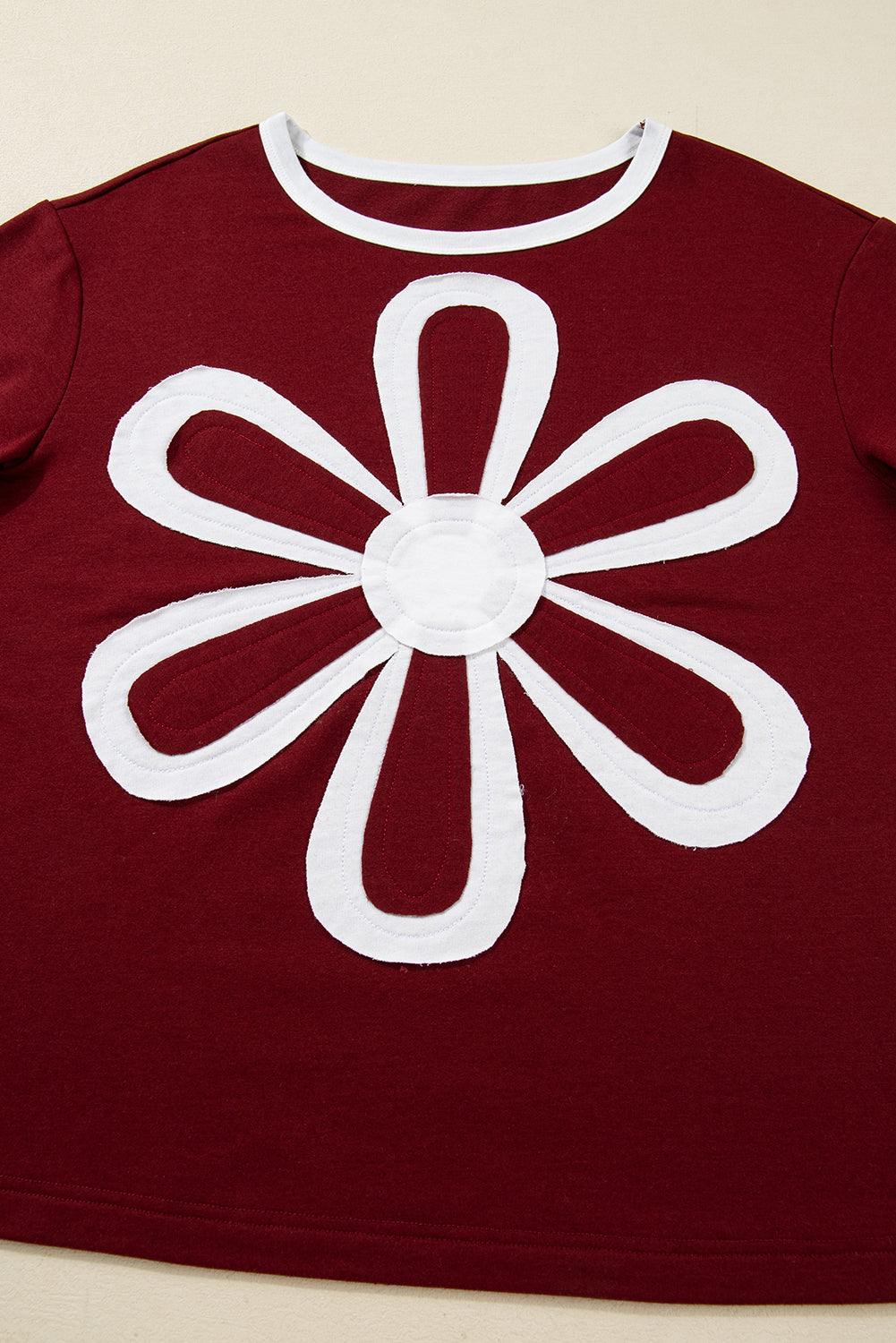 Red Dahlia women’s long sleeve top with round white contrast neckline, white sleeve bands, oversized daisy patch front, and relaxed shift silhouette.