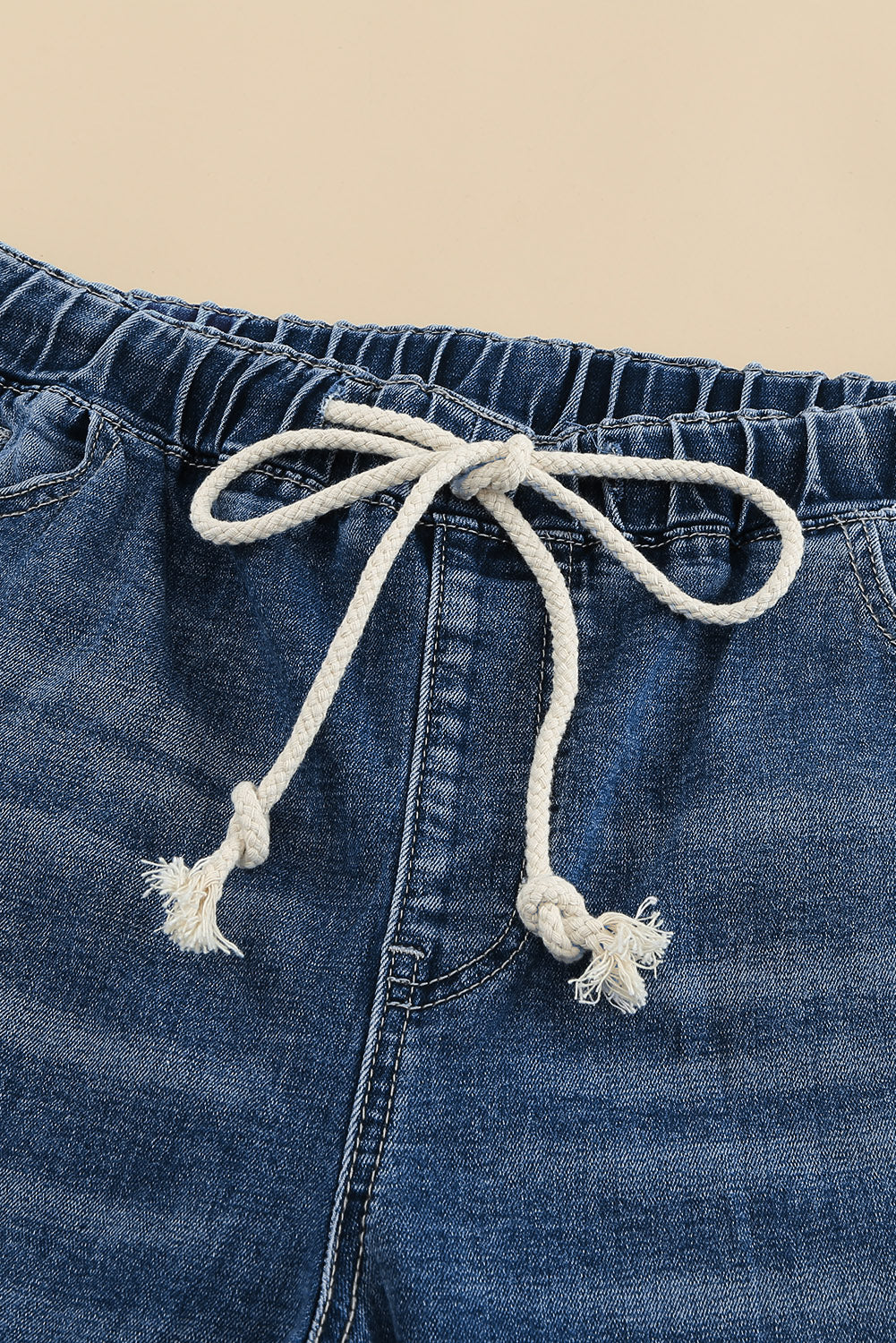 Medium wash blue distressed slim straight leg jeans with drawstring elastic waist and raw hem