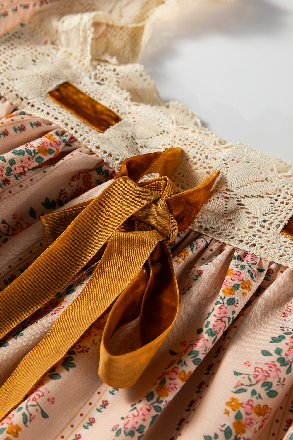 Blush floral babydoll mini dress with floral stripe print, cream lace-trimmed square neckline, brown velvet bow, and long sleeves.