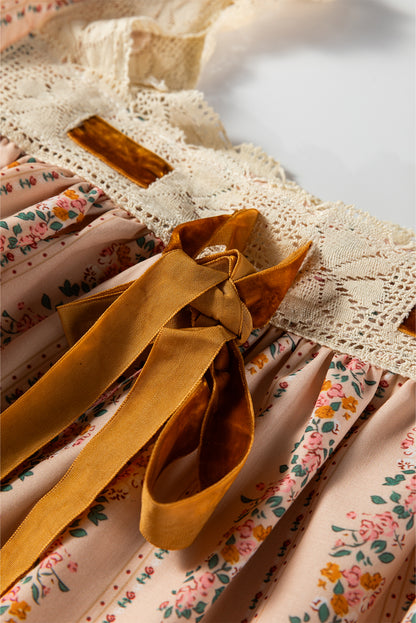 Blush floral babydoll mini dress with floral stripe print, cream lace-trimmed square neckline, brown velvet bow, and long sleeves.