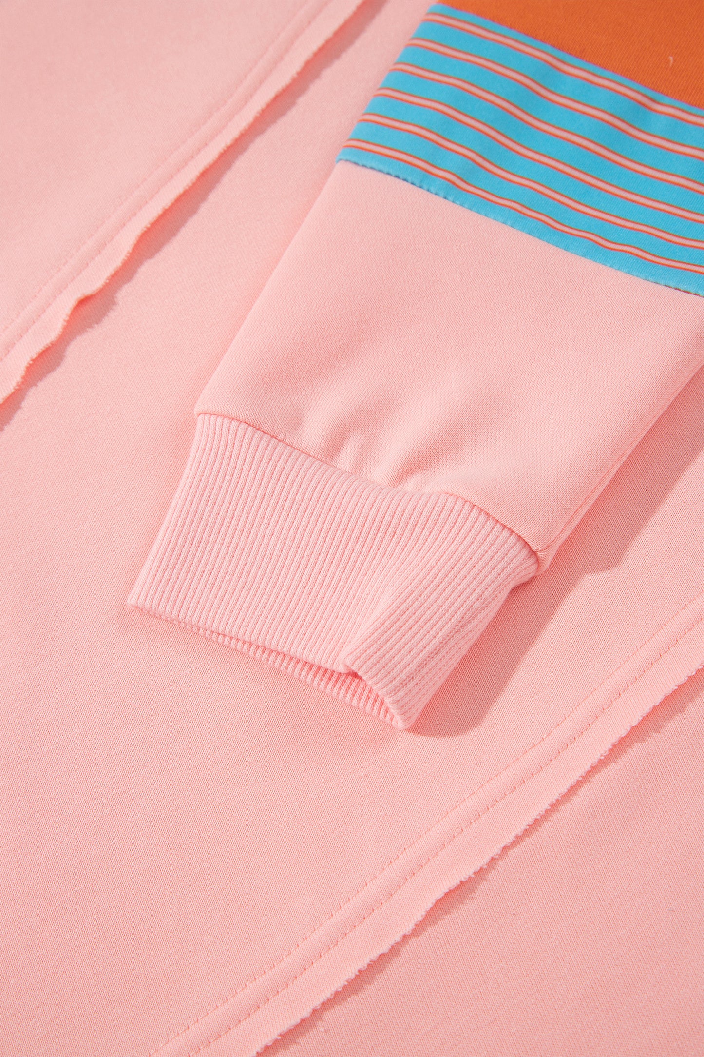 Pink crew neck long sleeve top with asymmetrical paneled body design and blue striped color block sleeves with contrasting orange accents.