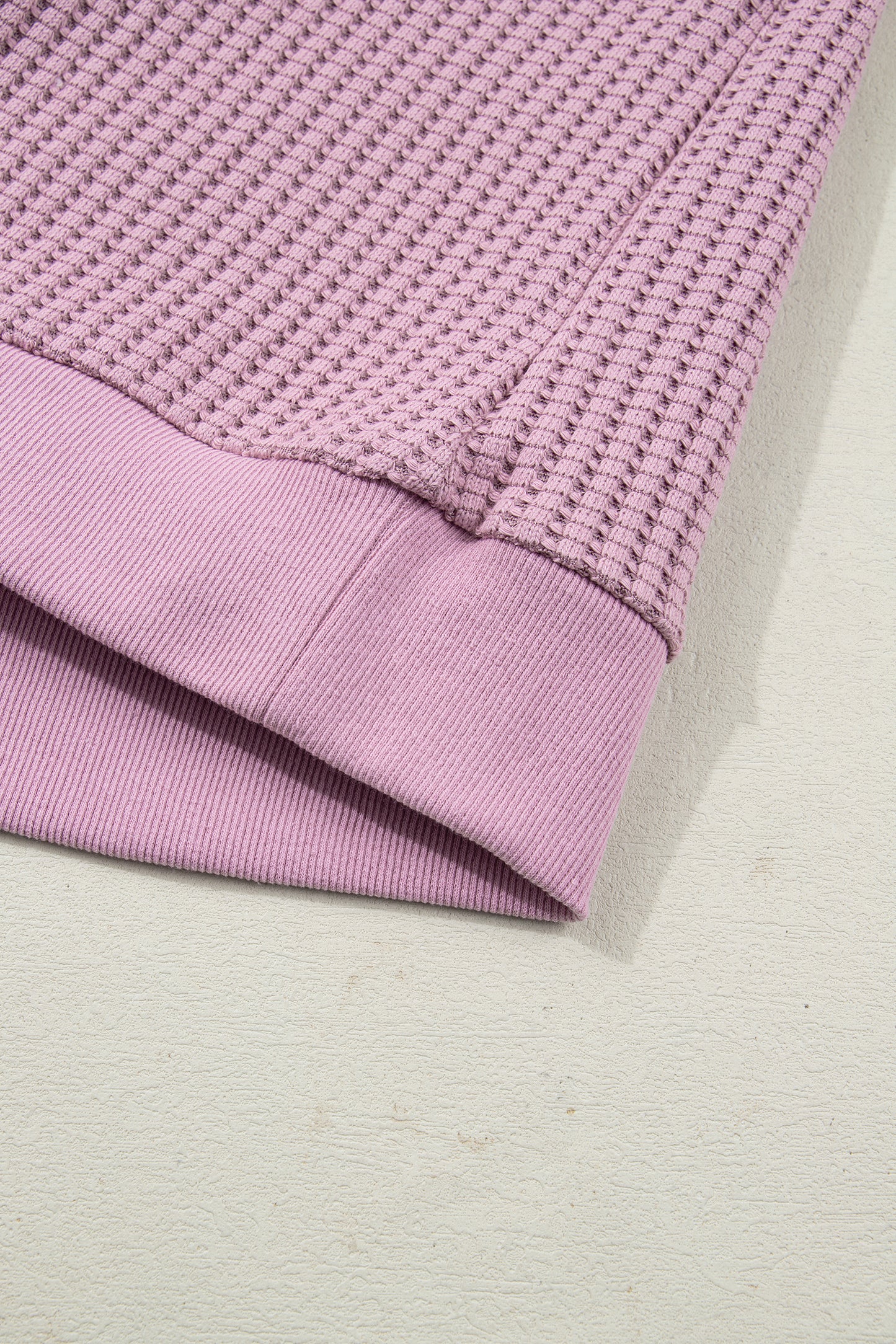 Woman wearing a Blush textured waffle knit pullover with snap collar, relaxed long sleeves, and ribbed cuffs with white pants.