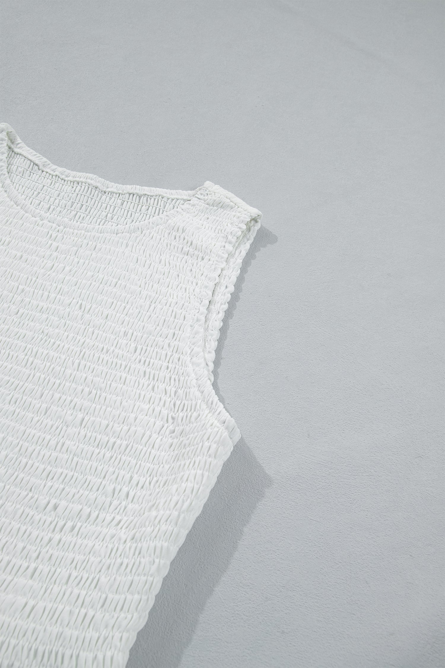 Women's white smocked sleeveless peplum top with embroidered eyelet hem, round neckline, textured bodice, and feminine boutique style.
