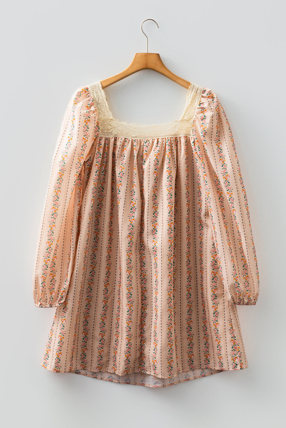 Blush floral babydoll mini dress with floral stripe print, cream lace-trimmed square neckline, brown velvet bow, and long sleeves.