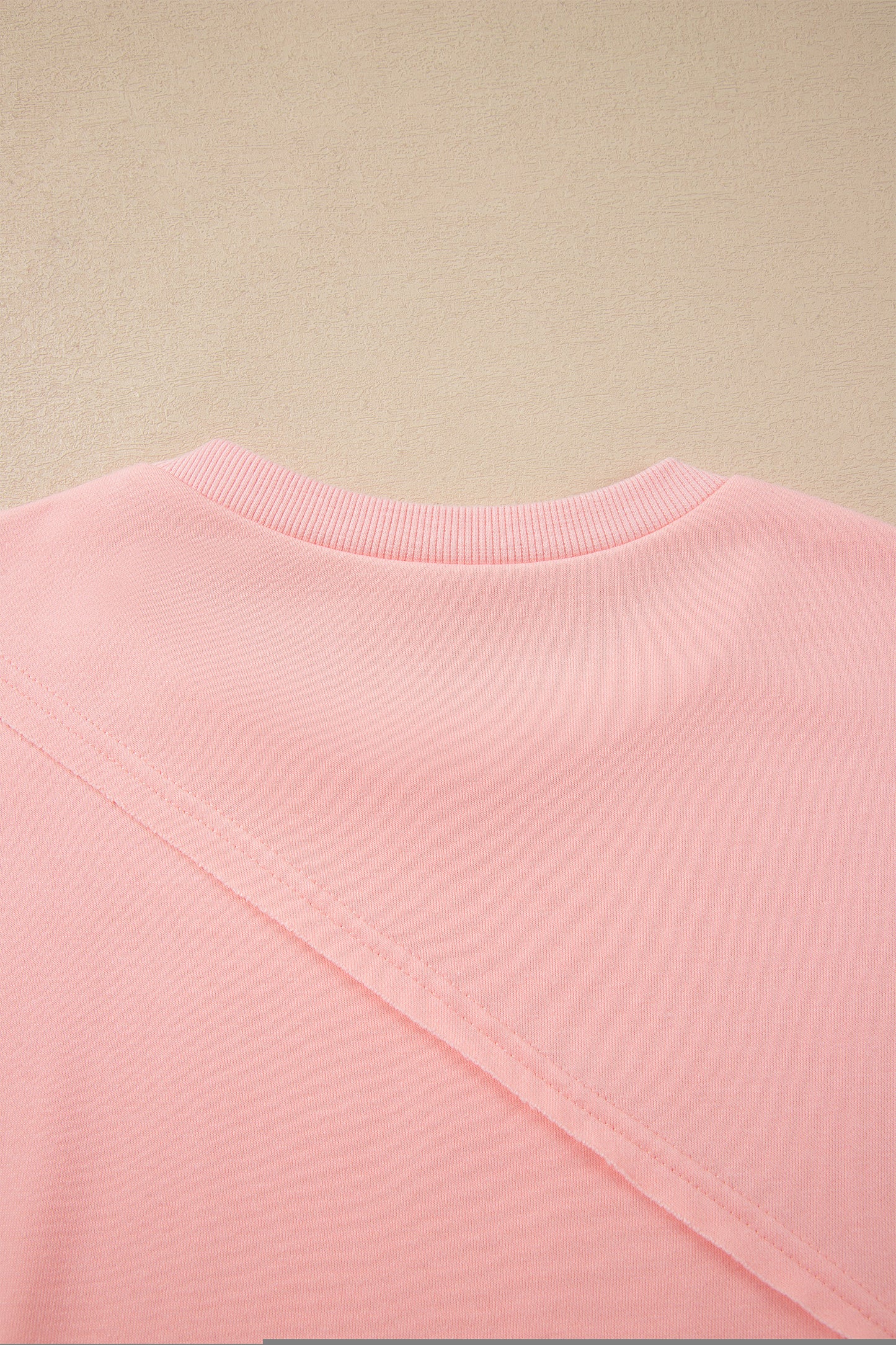 Pink crew neck long sleeve top with asymmetrical paneled body design and blue striped color block sleeves with contrasting orange accents.