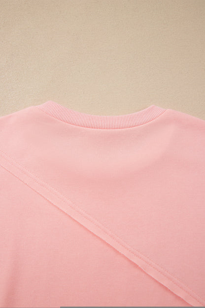 Pink crew neck long sleeve top with asymmetrical paneled body design and blue striped color block sleeves with contrasting orange accents.