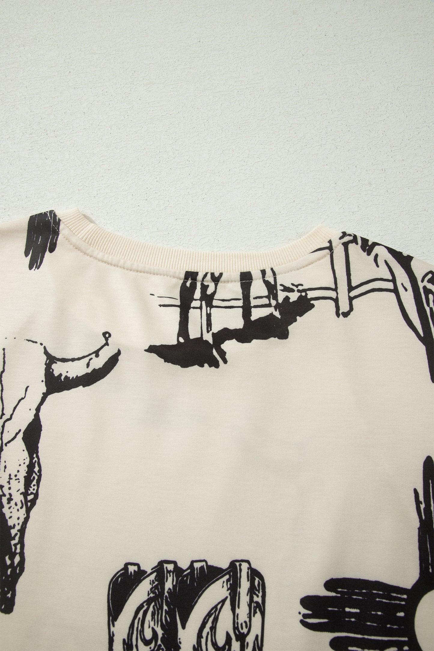 Cream Western graphic print top with crew neckline, short sleeves with gathered armholes, and black cowboy boot, cactus, horseshoe, and Southwestern motifs.