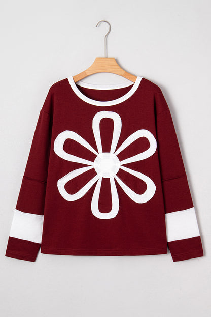 Red Dahlia women’s long sleeve top with round white contrast neckline, white sleeve bands, oversized daisy patch front, and relaxed shift silhouette.