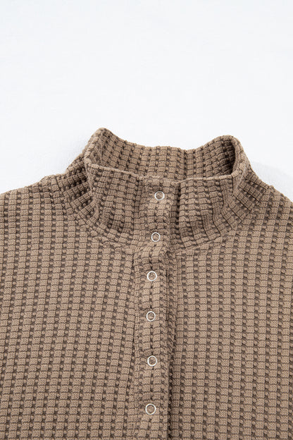 Woman wearing a Mocha textured waffle knit pullover with snap collar, relaxed long sleeves, and ribbed cuffs with white pants.