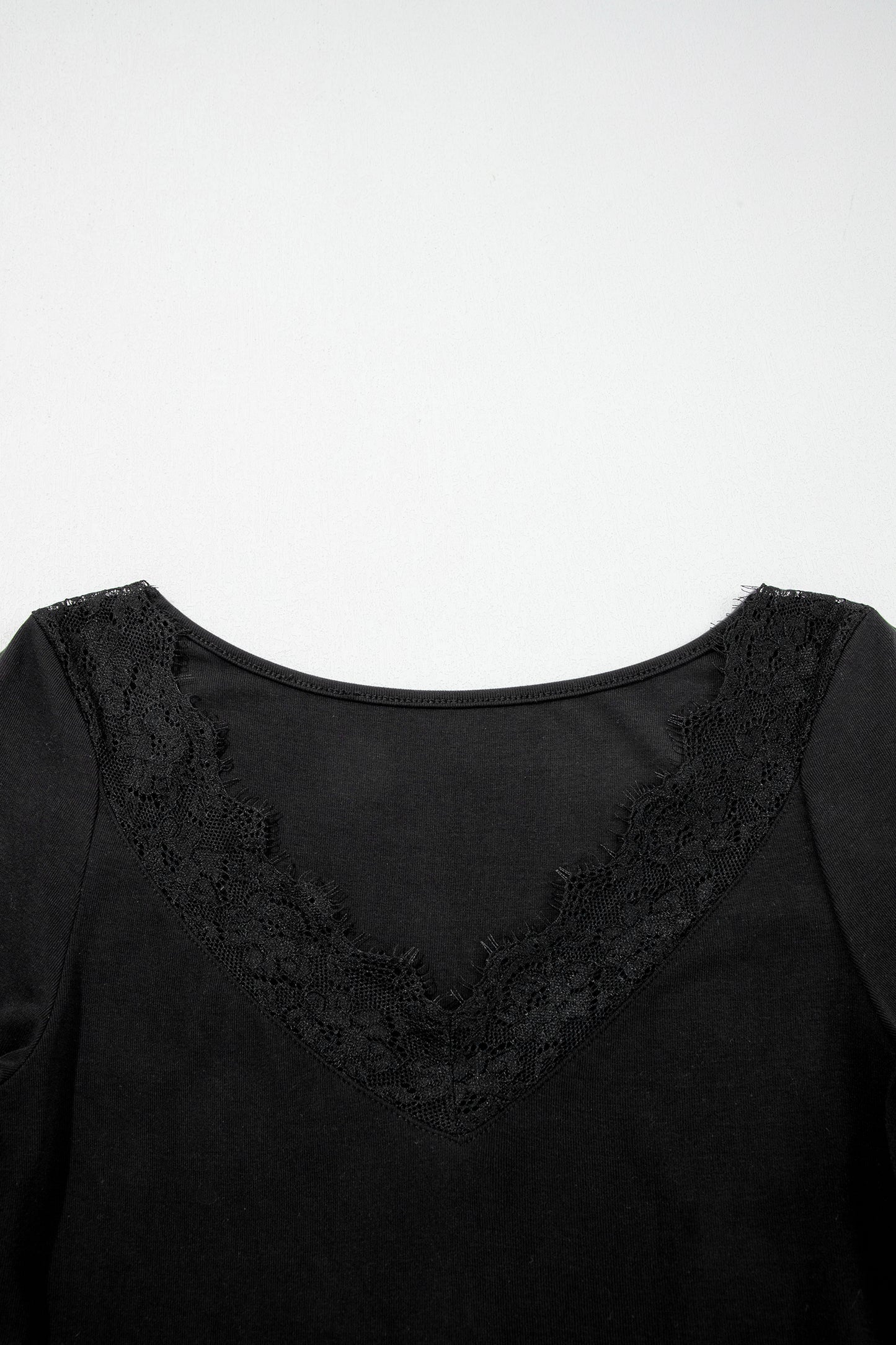 Black fitted long sleeve top with floral lace-trim V-neckline and soft stretch fabric styled with white pants.