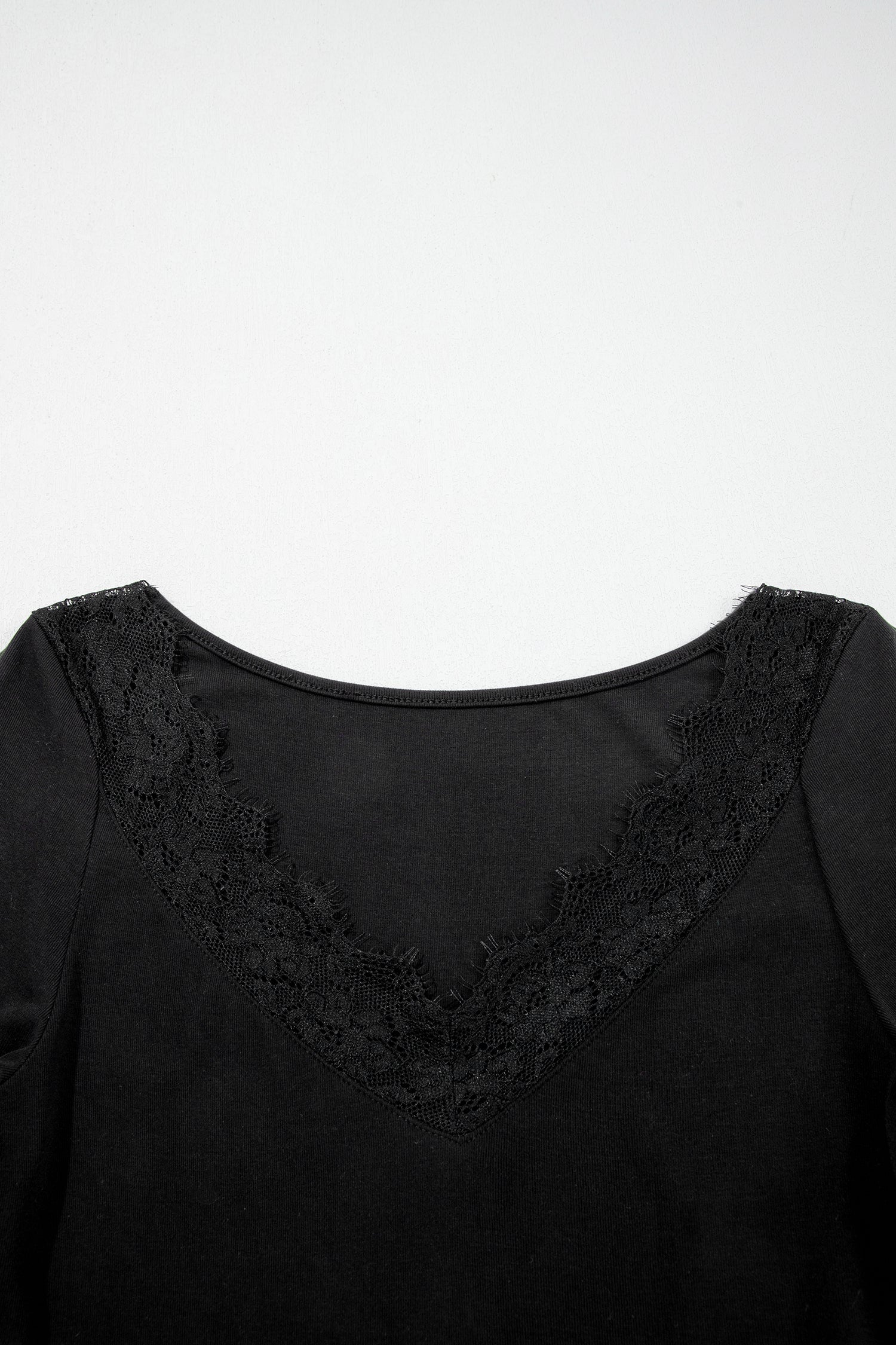 Black fitted long sleeve top with floral lace-trim V-neckline and soft stretch fabric styled with white pants.